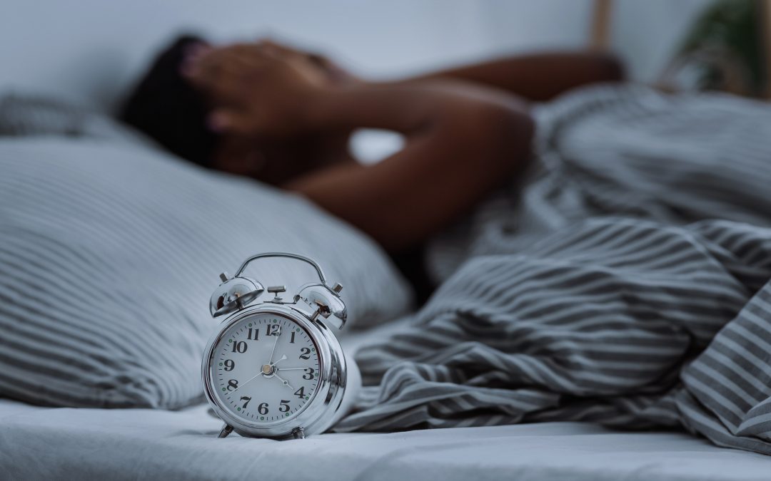 African american woman suffering from insomnia lying in bed without sleep with alarm clocks close up