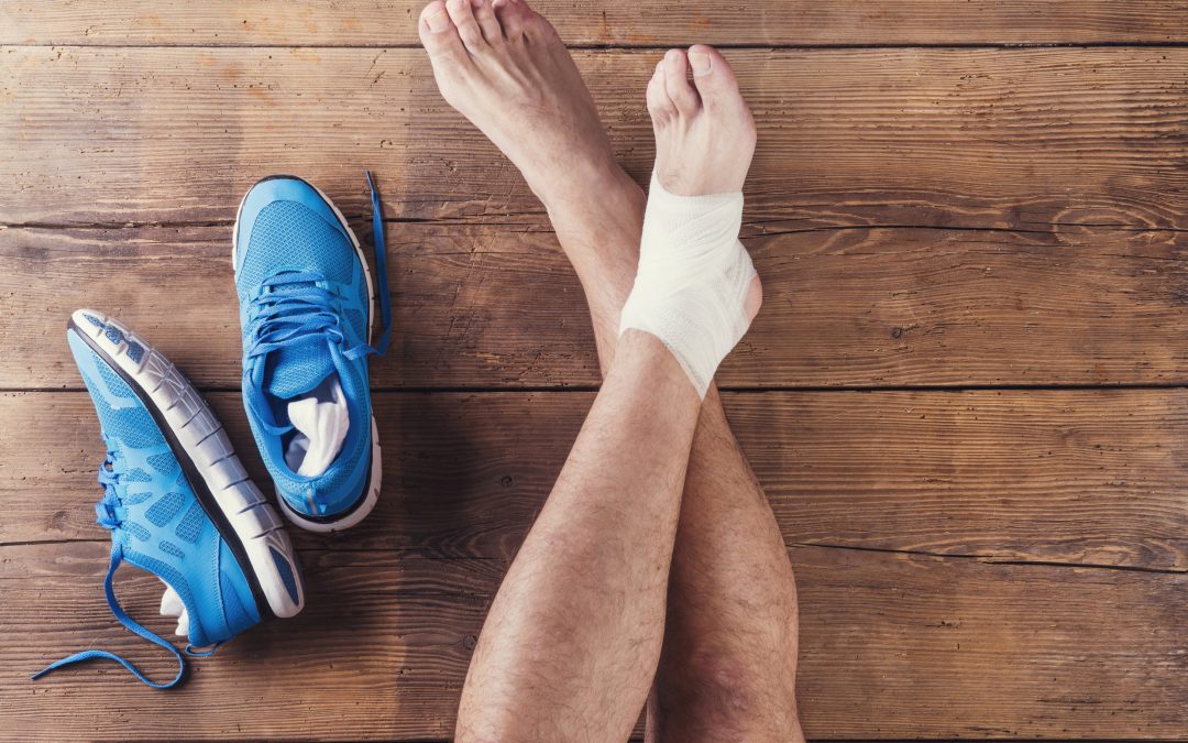 A pair of blue sneakers rests on the wooden floor beside a foot wrapped in a bandage,