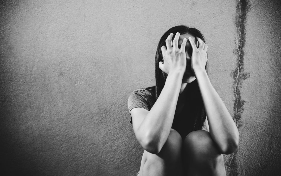 a young woman sits against a textured wall, her hands shielding her face as she grapples with her emotions