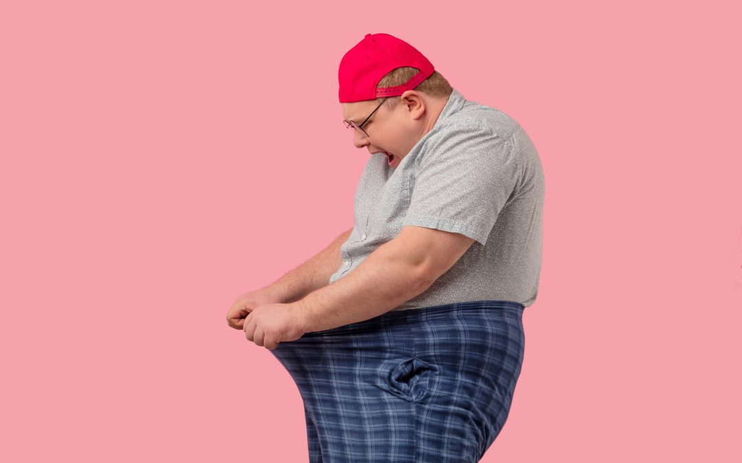 A comical moment captures a man in a bright red hat, playfully struggling with an oversized pair of pants.