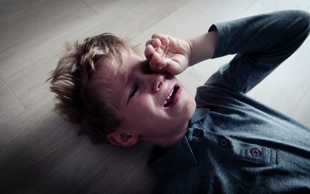 A young boy lies on the floor, tears streaming down his face