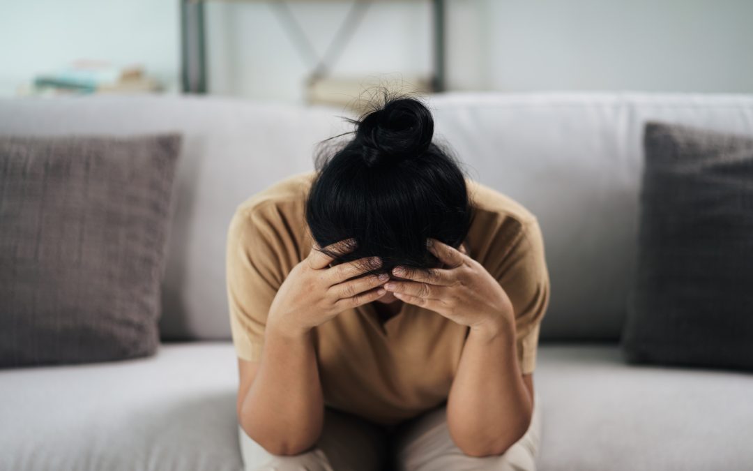 a woman sits on a cozy couch, her thoughts overwhelming her as she covers her face in reflection