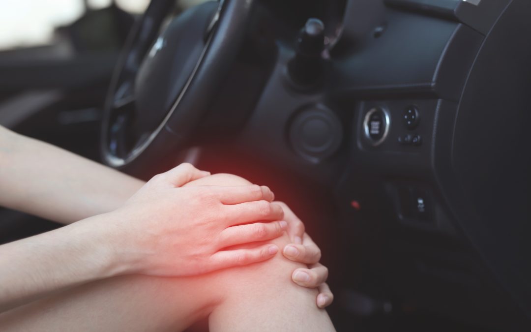 man sitting in a car holding his knee with pain